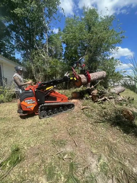The Ditch Witch mini skid steer removing tree debris from a back yard